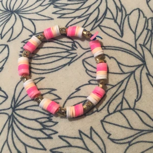  Handgjort färgglatt pärlarmband med stjärnor - Säljer ett handgjort armband med platta pärlor i rosa, vitt och ljusgult, varvat med små guldiga stjärnpärlor. Armbandet är elastiskt och har en lekfull vibe som passar perfekt till din stil. Längden är ca 16 cm och det är superenkelt att ta på och av.
