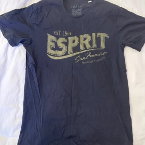 Mörkblå Esprit t-shirt med tryck - Snygg mörkblå t-shirt från Esprit med stort vintageinspirerat tryck i beige på bröstet där det står 'ESPRIT San Francisco EST. 1968'. Rund hals och klassisk passform, perfekt för dig som gillar streetwear och retro vibes.