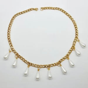 Guldhalsband med droppformade pärlor - Unikt halsband med chunky guldfärgad kedja och hängande droppformade vita pärlor. Kedjan har en klassisk karbinlås och pärlorna ger en lyxig och trendig vibe. Perfekt för dig som vill sticka ut med ett statement-smycke som drar blickarna till sig.