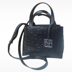 Svart handväska Armani Exchange - Snygg svart handväska från Armani Exchange med präglad logotyp över hela väskan och en silverfärgad metallbricka framtill. Väskan har både handtag och justerbar axelrem, perfekt för att bära på olika sätt. Tillverkad i skinn med stilren, fyrkantig form. Mått bredd: 16cm höjd: 22cm