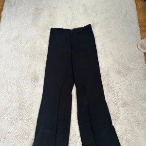 Svarta kostymbyxor Gina Tricot - Svarta kostymbyxor från Gina Tricot i klassisk rak modell. Byxorna har hög midja, dragkedja och knapp framtill. Perfekta till en snygg topp eller skjorta. Materialet känns mjukt och följsamt.