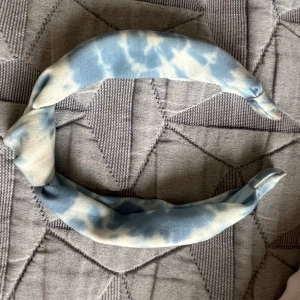 Blåvit tie-dye diadem - Snyggt diadem i mjukt tyg med blå och vita tie-dye mönster. Bred och lätt vadderad modell som ger en cool och avslappnad vibe. Perfekt accessoar för att lyfta din look med lite färg och stil.