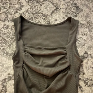 Ribbad grå kortklänning med drapering - Snygg ribbad grå klänning med ärmlös design och cool drapering framtill. Materialet är mjukt och stretchigt, vilket gör att den sitter bekvämt och följer kroppen. Perfekt för dig som gillar stilrena och trendiga plagg med lite edge.