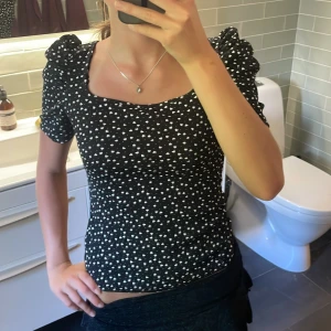 Svart topp med hjärtan - Supersöt svart topp med vita hjärtan över hela tyget. Toppen har puffiga korta ärmar och fyrkantig ringning. Figurnära passform och mjukt, stretchigt material som känns skönt mot huden. Perfekt för dig som gillar gulliga detaljer! Bra skick, passar som vanlig S storlek och den har inga defekter!!🤗