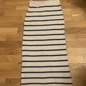 Vit långkjol med svarta ränder från H&M - Säljer en vit långkjol från H&M med svarta horisontella ränder. Kjolen har en rak passform, elastisk midja och en slits bak för extra rörelsefrihet. Materialet är mjukt och stretchigt, perfekt för en chill och stilren look.