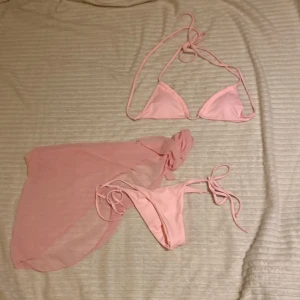Ljusrosa bikini med sarong=Rosa kjolen bredvid  - Supersöt ljusrosa bikini med trekantsöverdel och knyt i både topp och trosa. Matchande transparent sarong i samma färg ingår. Den är använd, har använts två gånger för att se hur den sitter så tvättning rekommenderars