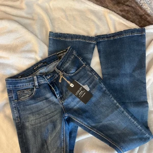 Blå bootcut jeans från Lexxury - Snygga blå jeans från Lexxury med klassisk femficksmodell och bootcut-ben. Jeansen har mid midja och är tillverkade i mjukt denimtyg med lätt tvättad look. Perfekta för dig som gillar en tidlös och avslappnad stil.