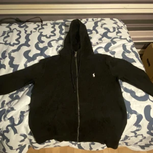 Svart hoodie från Polo Ralph Lauren ( M/S!) - ( STORLEKEN ÄR M MEN PASSAR S! )Svart hoodie från Polo Ralph Lauren med dragkedja framtill och klassisk huva med snörning. Tröjan har långärmade ärmar och den ikoniska Polo-loggan broderad på bröstet. Perfekt för chill dagar och enkel att matcha med jeans eller joggers. Kan diskutera priset, om du har något byte hör av dig.
