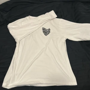 Vit långärmad tröja med statement-tryck - Säljer en vit långärmad tröja i mjuk bomull med svart handskrivet statement-tryck på ryggen: 'Social media is not real life'. På bröstet finns ett hjärtformat tryck med zebramönster. Perfekt för dig som gillar att sticka ut och vill ha en chill vibe.