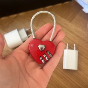 Rött hjärtformat kodlås - Säljer ett rött hjärtformat kodlås med silverfärgad vajer och detaljer. Perfekt accessoar för att låsa väskan eller skåpet och samtidigt visa lite kärlek. Låset har tre kodhjul och en liten silverhjärta i mitten.