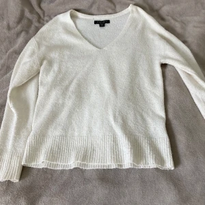 Vit stickad v-ringad tröja Amisu - Mysig vit stickad tröja från Amisu med v-ringning och långa ärmar. Tröjan har ribbade muddar vid ärmslut och nederkant, vilket ger en snygg och enkel look. Perfekt för lager-på-lager och passar till allt i garderoben.