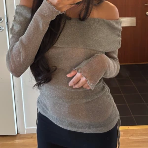Glittrig offshoulder topp  - Supersnygg glittrig silverfärgad offshoulder topp från Gina Tricot. Långärmad modell med croppad passform och volangdetaljer vid ärmslut. Tunn och stretchig syntetmix som sitter tight 