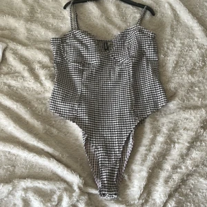 Ursnygg body - Supersnygg rutig body  från H&M Divided i svart och vitt. Modellen har smala axelband och högt skurna ben för en trendig look. Materialet är mjukt och stretchigt syntet som sitter bekvämt. Helt klart en perfekt body!
