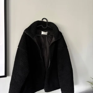 Svart teddyjacka från Carin Wester - Mysig svart teddyjacka från Carin Wester med hög krage och dragkedja framtill. Jackan har en fluffig och mjuk yta i teddy-material och är helfodrad på insidan. Perfekt för kyliga dagar när du vill ha både stil och komfort. Ordenarie pris: 799kr💕