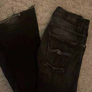 Svarta jeans från Nudie Jeans Co - Säljer ett par svarta jeans från Nudie Jeans Co med klassisk femficksdesign och snygga kontrastsömmar på bakfickan. Jeansen har en mörk tvätt och är tillverkade i slitstarkt denim. Perfekta för dig som gillar en stilren och tidlös look. Jag googlade å ett par sånna här jeans från det här märket går på 1600 egentligen ”Lite förstörda där nere där man går” 