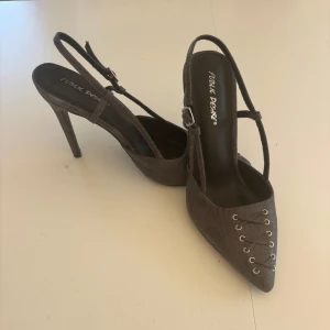 Gråa klackskor  med snörning från Public Desire - Snygga gråa pumps från Public Desire med spetsig tå och cool snörningsdetalj framtill. Skorna har hög klack och smala remmar med spänne runt hälen. 