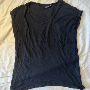 Svart t-shirt med ficka KappAhl - Svart t-shirt från KappAhl med rund halsringning och en bröstficka. Modellen är kortärmad och har en loose passform som känns chill och enkel. Materialet är mjuk bomull, perfekt för en avslappnad stil.