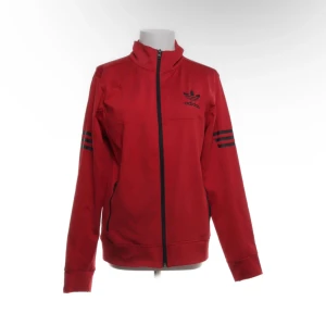 Röd Adidas vindjacka med svarta detaljer - Röd vindjacka från Adidas med svarta dragkedjor och klassiska svarta ränder på ärmarna. Jackan har hög krage, lång ärm och Adidas-logga på bröstet. Perfekt för en sportig look och enkel att matcha med jeans eller träningsbyxor. Storlek L, endast testad💞