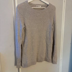 Ljusgrå/beige tröja från H&M - En enkel och stilren ljusgrå/beige tröja från H&M. Tröjan har rund hals, långa ärmar och ribbade muddar vid hals, ärmslut och nederkant. Perfekt för dig som gillar en clean look och vill ha något mjukt och bekvämt till hösten eller vintern.