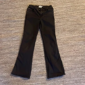 Svarta bootcut jeans med fickor - Snygga svarta jeans med bootcut passform och klassiska fem fickor, inklusive bakfickor med knappdetalj. Byxorna har normal midja och är tillverkade i ett mjukt jeansmaterial som sitter skönt. Perfekta för dig som gillar en stilren look med lite extra edge.