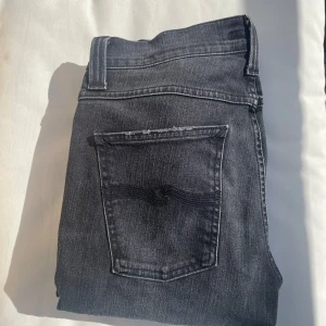 Svarta Nudie jeans med slitningar och fade - Dags o sälja vidare mina unika svarta Nudie jeans med exemplariska slitningar och unik look. Finns inte några sprillans nya identiska brallor som dessa på marknaden då modellen släpptes vid enbart 1 tillfälle. Skicket är på topp, använda men väl omhändertagna så inga tecken alls! Strl 30/32. Priset ligger väldigt lågt i relation till liknande jeans med sån här stil! Hör av er vid frågor!