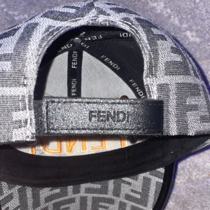 Fendi keps med FF-mönster - Snygg keps från Fendi med ikoniskt FF-mönster i grått och svart. Framtill är FENDI ROMA broderat i gult och vitt. Justerbar rem bak med Fendi-logga. Materialet är troligtvis bomull eller polyester, perfekt för dig som gillar lyxiga accessoarer.