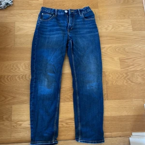 Blå tapered jeans från H&M, relaxed fit - Säljer ett par blå jeans från H&M med relaxed fit och tapered ben. Jeansen har justerbar midja och klassisk femficksdesign. Perfekta för dig som gillar en avslappnad men ändå snygg look. Passar dig som är 12-13 år.