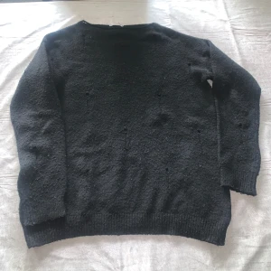 Svart stickad tröja med rund hals - En enkel svart stickad tröja med rund hals och långa ärmar. Tröjan har en klassisk passform och ribbade muddar vid ärmslut och nederkant. Perfekt för att hålla värmen under kyliga dagar.