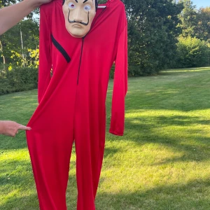Röd helkroppsdräkt med huva S/M - Cool La Casa De Papel dräkt som jag köpt på Vinted så vet inte vart den kommer ifrån. Perfekt för maskerad eller temafest! Mask ingår. På masken är det några repor som man ser på sista bilden men annars är dräkten bra.