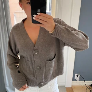 Grå kofta med stora knappar - Mysig grå kofta med v-ringning och tre stora knappar framtill. Modellen är loose fit och har två praktiska fickor på framsidan. Materialet är stickat och känns mjukt mot huden. 