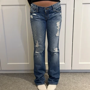 Blå bootcut jeans Abercrombie & Fitch - Snygga blå jeans från Abercrombie & Fitch med bootcut passform och slitna detaljer framtill. Klassisk femficksmodell med låg midja och broderade bakfickor. Tillverkade i jeansmaterial med coolt distressed look. Midjemått: 37 cm Innerbenslängd: 84 cm