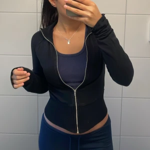 Svart croppad kofta - Säljer en svart, croppad kofta med lång ärm och dragkedja framtill. Jackan har en tight passform och ribbade detaljer vid midjan. Perfekt för dig som gillar sportig och stilren look. Från Nelly💗