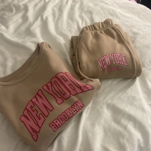 Beige mjukis set  - Beige mjukis set från Shein i storlek M med tryck i rosa och rött där det står 'New York Brooklyn' på bröstet. Tröjan har långa ärmar och rund hals. Materialet är mjuk polyester, perfekt för chill dagar och streetstyle.