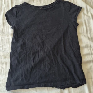 Svart basic t-shirt från H&M - En svart, enkel t-shirt från H&M Basic i ekologisk bomull. Modellen har rund hals och korta ärmar, med en normal passform som sitter skönt. Perfekt för chill dagar och passar till allt. Materialet är mjukt och andas bra.