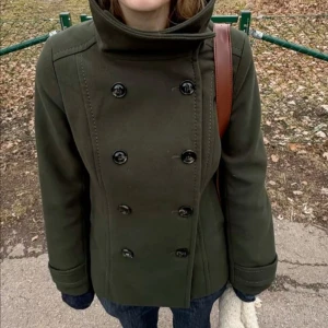 Mörkgrön skepparkavaj med hög krage - Snygg mörkgrön skepparkavaj med dubbelknäppning och hög krage. Jackan har långa ärmar och markerade sömmar för en clean look. Perfekt för dig som gillar klassisk stil med en twist. Passar till både jeans och dressade byxor.