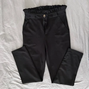 Svarta högmidjade byxor från Shein - Snygga svarta byxor från Shein med hög midja och rynkad kant upptill. Byxorna har raka ben, sidfickor och stängs med knapp och dragkedja. Materialet är mjukt och har en lätt glansig finish som ger en clean look.