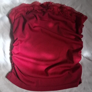 Röd ribbad tubtopp med spets och rosett - Supersöt röd tubtopp med ribbad struktur och bred spetskant upptill. Toppen har en liten rosett framtill som extra detalj. Färgen är mest som på sista bilden. Aldrig använd men jätte fin! Antingen XS eller S