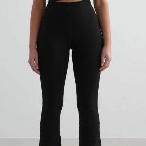 Svarta höga leggings med bootcut - Svarta leggings med hög midja och bootcut-snitt. De är tighta upptill och släpper ut vid anklarna för en snygg siluett. Perfekta för dig som gillar en clean och stilren look. Tillverkade i stretchigt syntetmaterial för maximal komfort. Nypris: 799kr