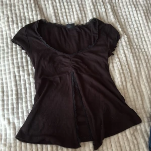Svart topp med spets från Gina Tricot - Supersöt svart topp från Gina Tricot i storlek XS. Modellen har korta ärmar, v-ringning med spetskant och en snygg rynkdetalj framtill. Tyget är mjukt och stretchigt, perfekt för en trendig look. Passar dig som gillar feminina detaljer och enkel stil. Toppen är inte röd det ser bara ut så på bilden.
