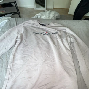 Ljusgrå Tommy Hilfiger tröja XL - Säljer en ljusgrå långärmad tröja från Tommy Hilfiger i storlek XL. Tröjan har rund hals och ett stilrent tryck med logga och texten 'EST. 1985' på bröstet. Mjuk bomullskvalitet som är skön att ha på sig och passar perfekt till jeans eller joggers.