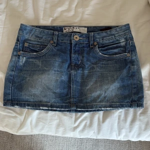 Blå jeanskjol från Diverse Denim - Snygg blå mini jeanskjol från Diverse Denim med klassisk femficksdesign, slitna detaljer och rå kant nedtill. Kjolen har knapp och dragkedja framtill samt dekorativa sömmar på bakfickorna. Storlek 28 men den är inte så stretchig💗
