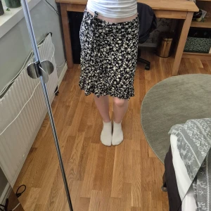 Svart blommig kjol - Snygg svart kjol med vita blommor och volangdetaljer. Perfekt för en somrig look. I stl 134- 140 men på bilden ser ni mig ha på den (som valigtvis bär stl S) så den passar många. Funkar att ha både lowwaist och highwaist samt allt där emellan:) Använd endast en gång.