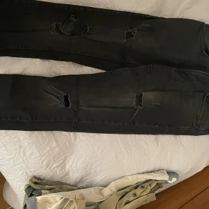 Svarta jeansbyxor från Rebel - Snygga svarta jeansbyxor från Rebel med slitna detaljer för en cool look. Byxorna har en normal passform och är tillverkade i ett bekvämt jeansmaterial. Perfekta för en avslappnad stil.