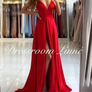 Röd långklänning från Dressroom Linné - Elegant röd långklänning med djup v-ringning och slits. Klänningen har smala axelband och en öppen rygg med snörning. Perfekt för en glamorös kväll.