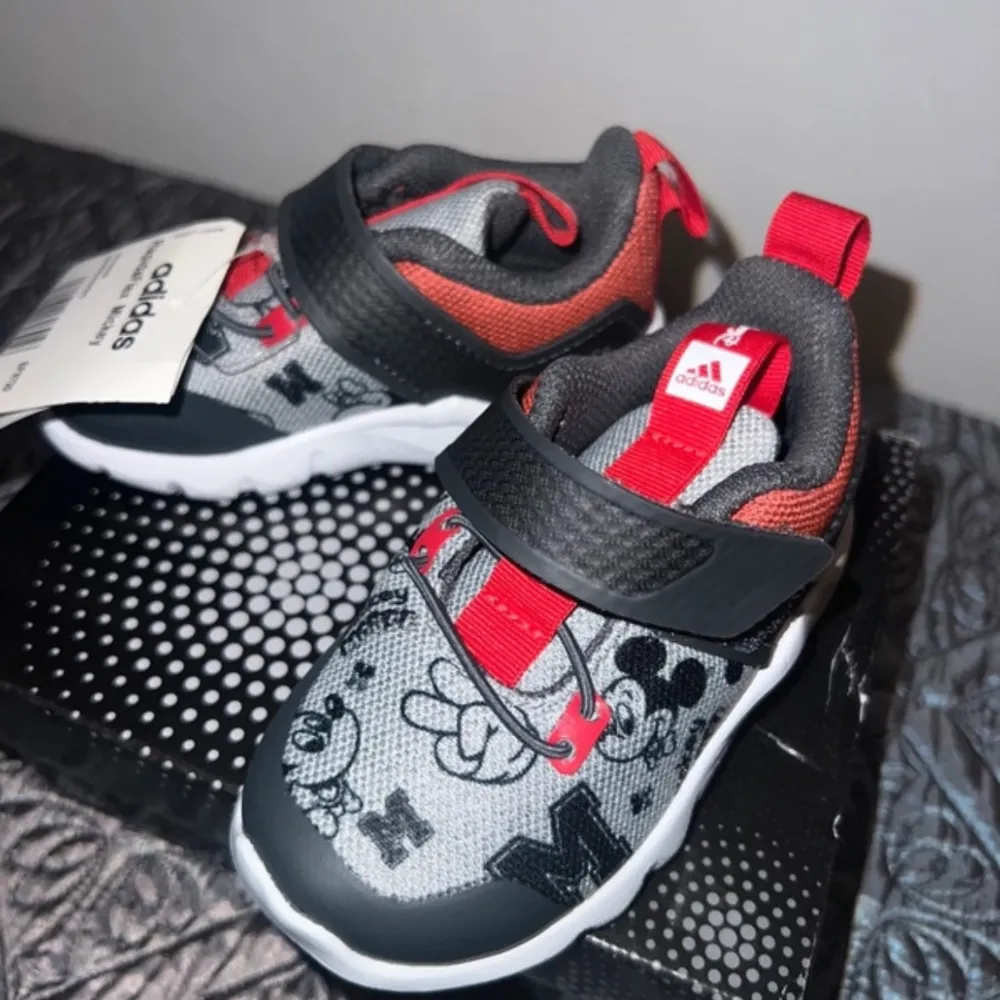 Snygga och lekfulla barnskor från Adidas med Disney-motiv. Skorna har en grå bas med svarta och röda detaljer samt ett mönster av Disney-figurer. De har en praktisk kardborreknäppning och en bekväm vit sula. Helt nya. Storlek 20. . Kengät.