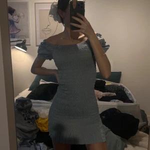 Grå/blå offshoulder klänning - Säljer en stilren grå offshoulder klänning med smockdetaljer. Klänningen har kort längd och puffiga ärmar. Kommer passa en xxs/xs. Jag är 167 cm lång. 