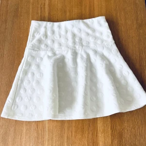Vit prickig kjol från H&M - Snygg vit kjol från H&M med prickigt mönster och dragkedja bak. Perfekt för en stilren look. Märkt st 170, passar  även S. Midja: 2 x 36 cm, dragkedja bak. Längd 45cm.
