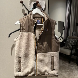 Fleece väst från k-way - Säljer en snygg beige och brun väst från K-Way. Västen har en dragkedja framtill och är tillverkad i fleece. Perfekt för lager-på-lager under kyligare dagar. 🧥
