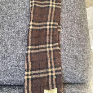 Brun rutig halsduk från Burberry - Säljer en klassisk brun rutig halsduk från Burberry. Den har ett tidlöst mönster med inslag av beige och svart. Perfekt för våren 