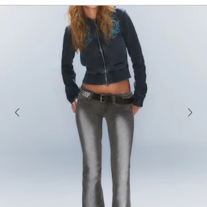 Svart bomberjacka med broderi - Snygg svart bomberjacka med dragkedja och coolt broderi på axlarna. Jackan har långa ärmar och en croppad passform som ger en trendig look. Perfekt för att lyfta din outfit!